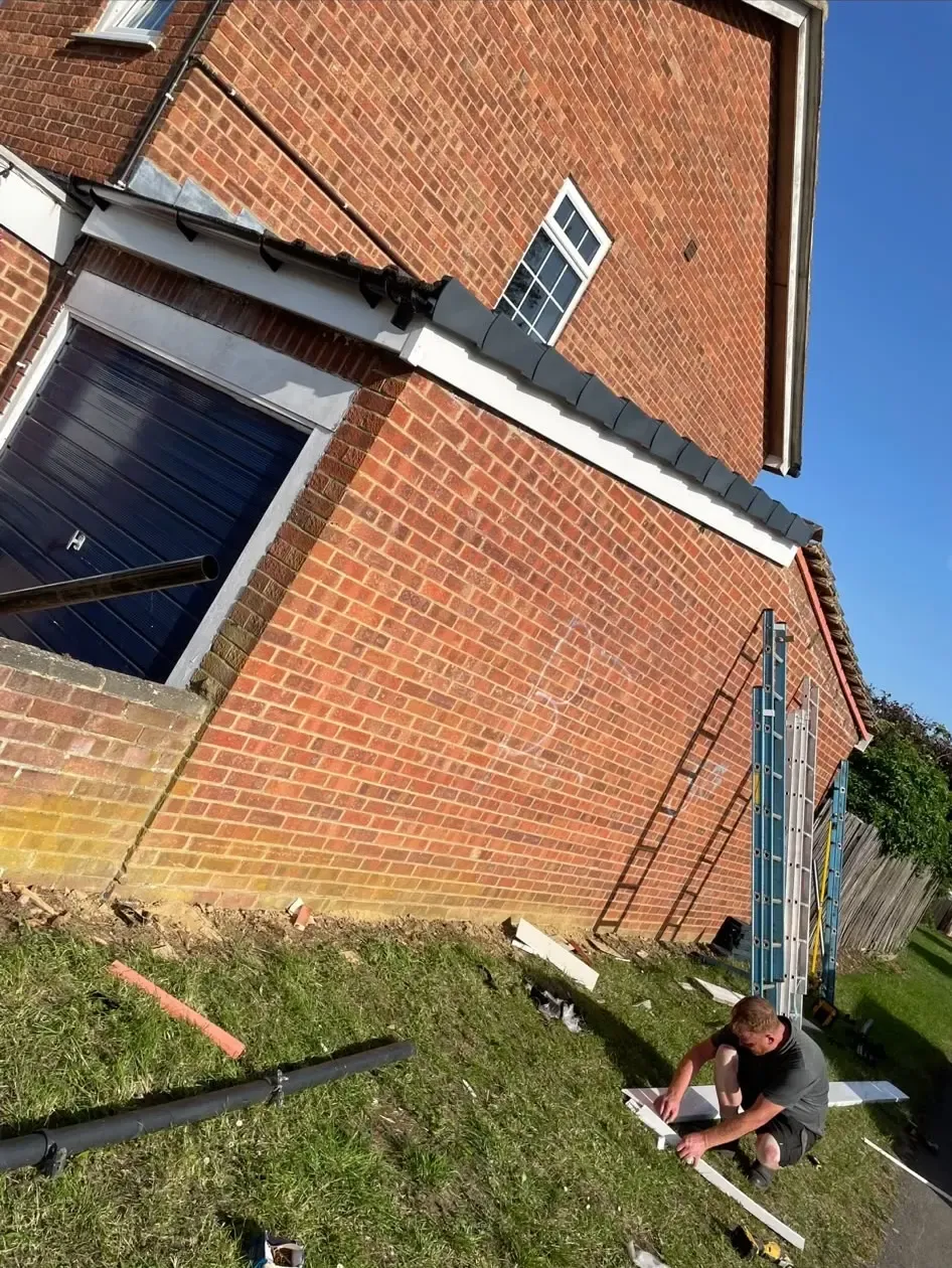 Tradesman fitting new white uPVC fascia and soffit boards to a brick house roofline