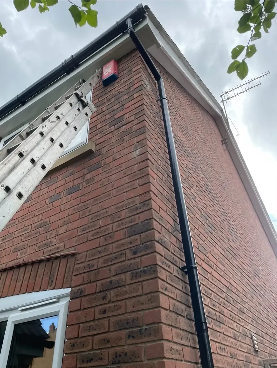 Newly installed black uPVC guttering and downpipe on a brick house