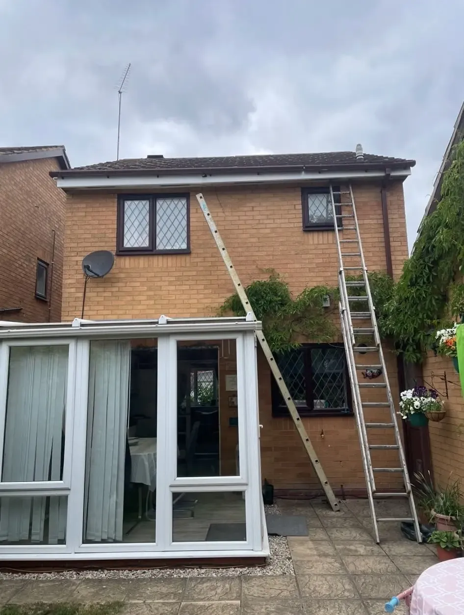 Two ladders leaning against a brick house reaching up to the roofline and gutters.