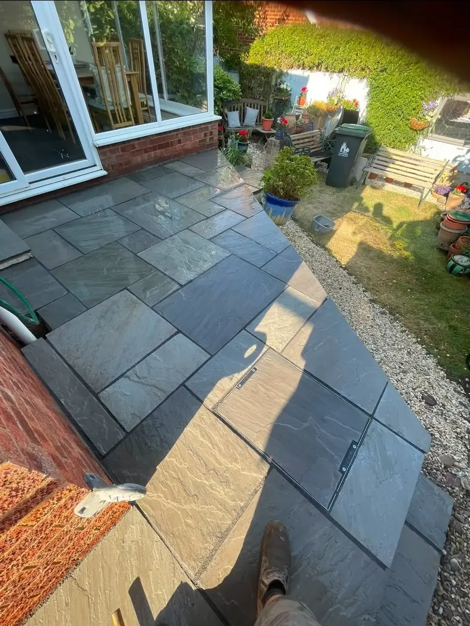 Newly installed grey natural stone patio with a seamlessly integrated recessed manhole cover outside a home in Northampton.