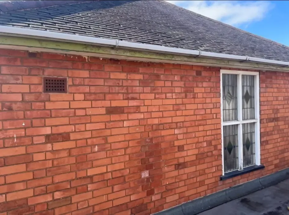 Exterior red brick wall of a property showing a window, guttering, fascia, and pitched roof