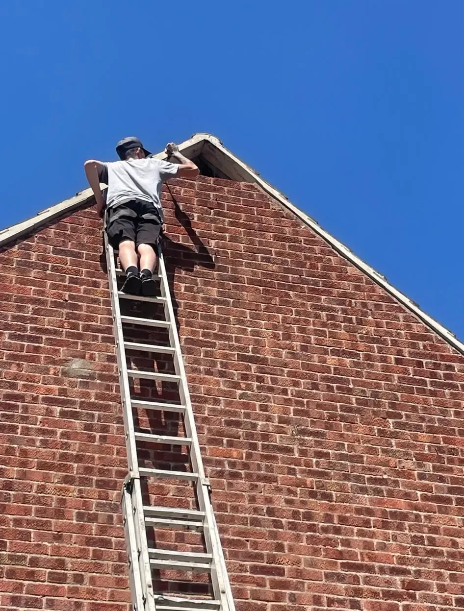 Local roofer on a tall ladder working on the apex of a brick house in Northampton